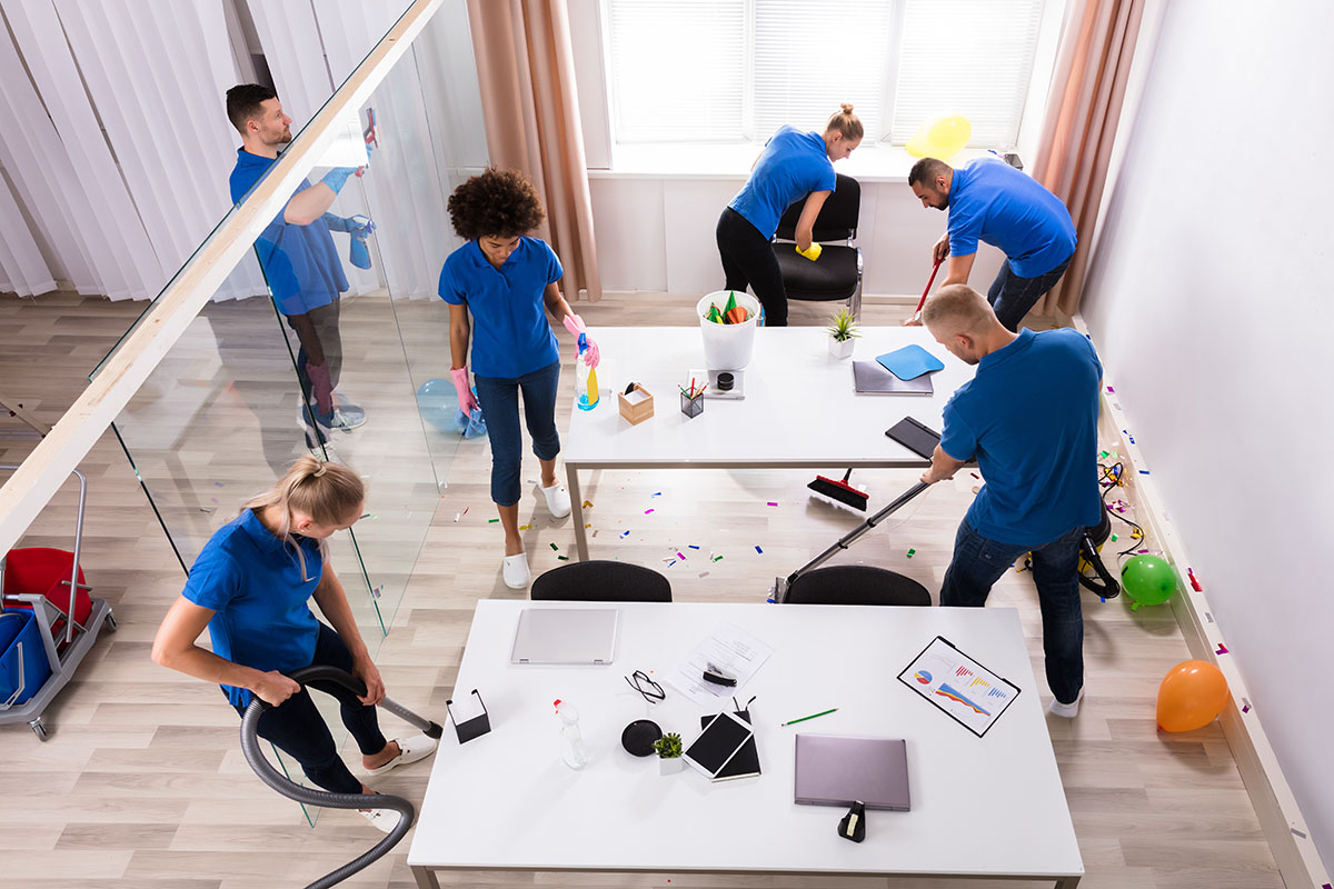 Group Of Young Janitors Cleaning Office With Cleaning Equipment After Party